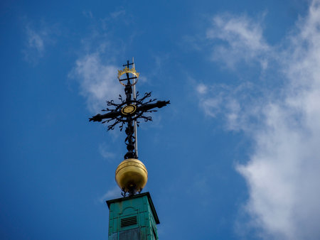 Green patina church dome with golden sphere and elaborate orthodox cross under blue skyの写真素材