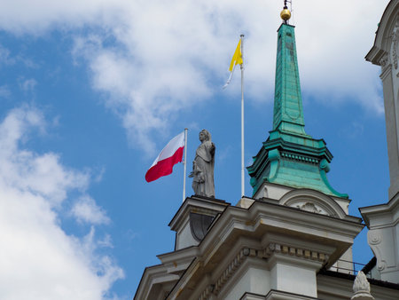 Historic church tower with green patina dome and Polish flag against cloudy blue skyの写真素材