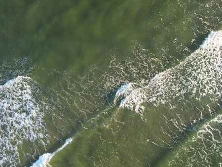 Aerial view of pristine ocean waves crashing against rocky coastal shore creating white foam patternsの写真素材