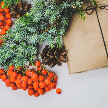 Pine Cones, Red Berries, Spruce Branches And Gift Kraft Box. Christmas and New Year's Decor With Toy Deer. Vintage Style Flat Lay Holiday Composition White Background Copy Spaceの写真素材