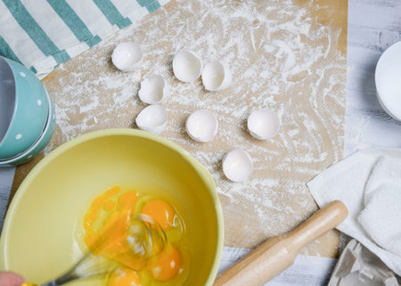 Table with ingredients for dough, raw eggs, flour, plate, napkins, rolling pin and whisk. Process of...