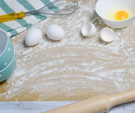 Table with ingredients for dough, raw eggs, flour, plate, rolling pin and whisk. Process of...