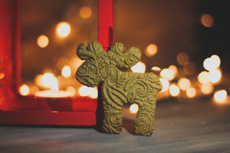 Gingerbread cookie and Christmas decorations on a table. Festive blurred lights, red candle and...