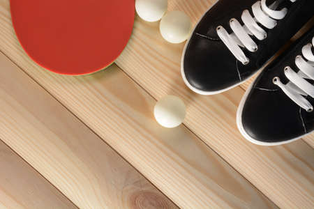 Table tennis racket, balls and black sneakers with white laces on a wooden backgroundの写真素材