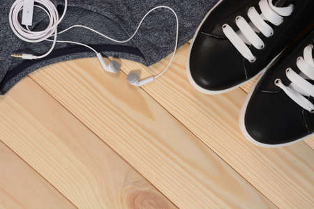 Running set. Black sneakers, shirt and headphones on a wooden background close upの写真素材