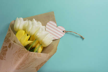 Beautiful yellow and white tulips with heart card in wrapping paper on a light turquoise backgroundの写真素材