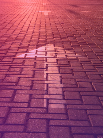 Arrow on a road tile in the rays of the setting sun on purple toned blurred background