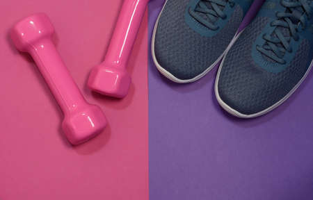 Sport sneakers and womens dumbbells on pink purple background with copy space for text. Sport objects background. Sports conceptの写真素材