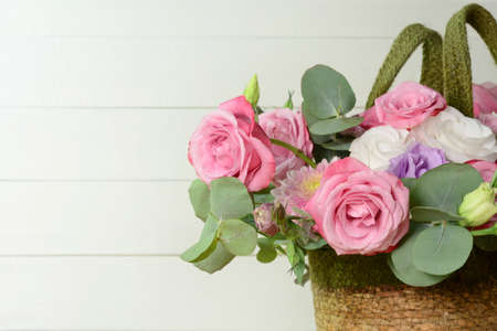 Bouquet of pink roses in basket on white wooden background closeup. Roses and eustoma flowers greeting card, floristics, wedding, flower shop, holidayの写真素材
