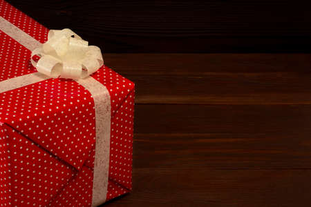 Gift box of red color with white ribbon on dark brown wooden backgroundの写真素材