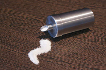 Tipped over sugar dispenser with sugar pile on brown wooden tableの写真素材