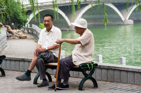 Two senior Chinese men chat sitted on a benchのeditorial素材