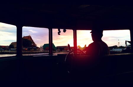Sunset Bangkok riverside view from silhouetted backlit-boat's windowの写真素材