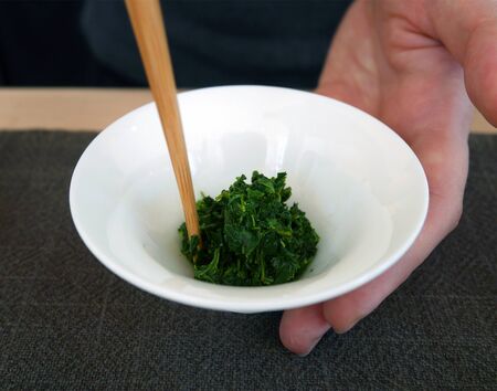 Stir fresh green tea leaves in white cup with chopsticksの写真素材