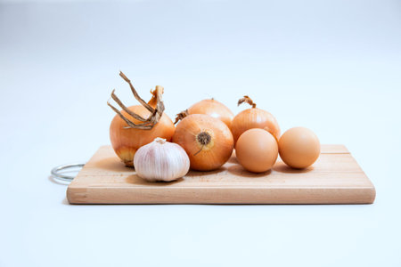 onion, garlic and eggs on a cutting board on a white background