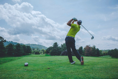 golfer hitting shot with club on golf course in beautiful landscape