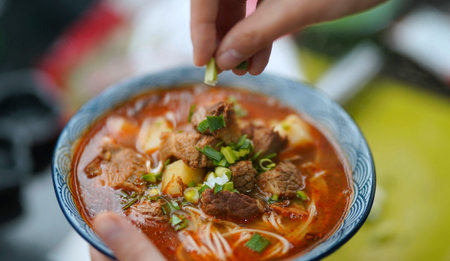 Close-up of a woman's hand holding a bowl of spicy beef noodle soup