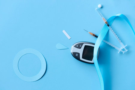 Glucose meter, syringe and blue ribbon on blue background