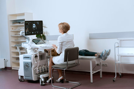 Female doctor looking at x-ray monitor while sitting on chair in clinic