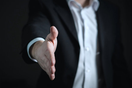 Businessman offering handshake on dark background. Focus on the hand.