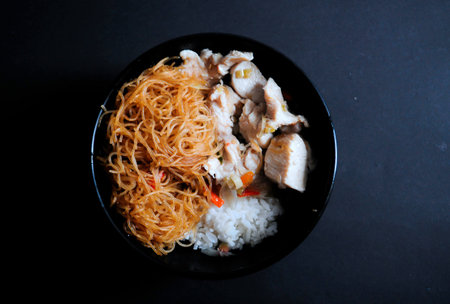 Rice noodles with chicken and vegetables in black bowl on black background