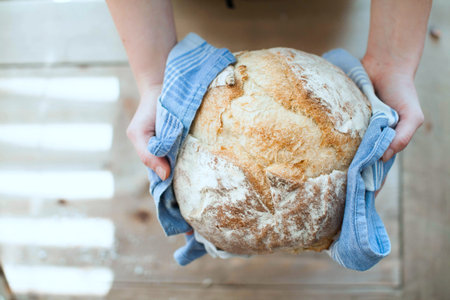 Female hands holding a freshly baked loaf of bread in the kitchen.の写真素材