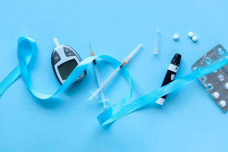 Glucose meter, syringe, pills and blue ribbon on blue background