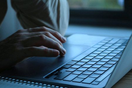 Man working on laptop in home office, close-up of hands