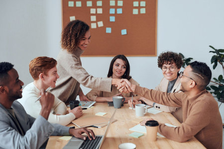 businesswoman shaking hands with multicultural colleagues during meeting in office, teamwork concept