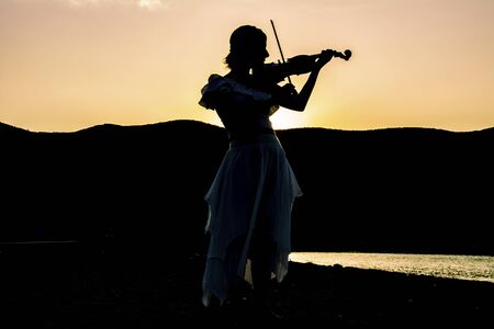 Silhouette of woman playing violin at beachの写真素材