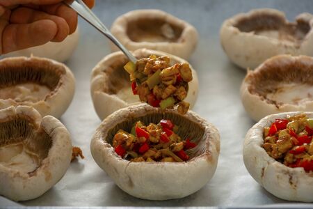 A hand filling the empty mushrooms on the baking paper with the stuffing insideの写真素材