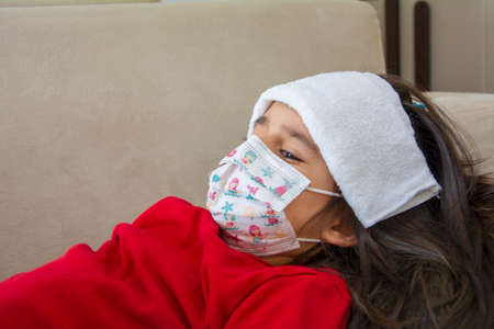 A man's hand covers a wet cloth on the head of the girl who is ill in close-upの写真素材
