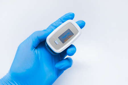 Doctor hand in protective medical gloves holding modern fingertip pulse oximeter on a white background, closeupの写真素材
