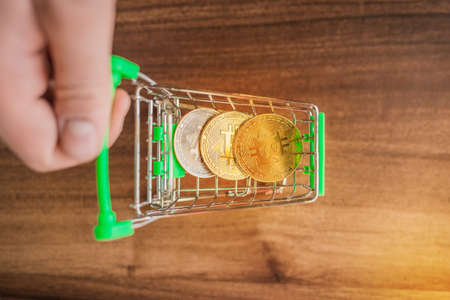 A businessmans hand rolls a shopping basket with bitcoins on a wooden table. Cryptocurrency and bitcoin concept, top viewの写真素材