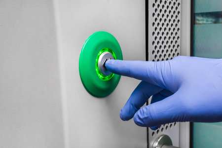 A man's hand in a protective medical glove presses the door control button in a modern electric...