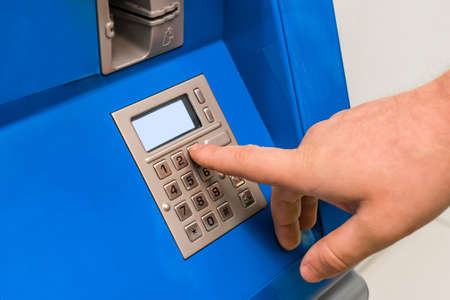 A man's hand dials a pincode at the terminal for issuing money, close-up.の写真素材