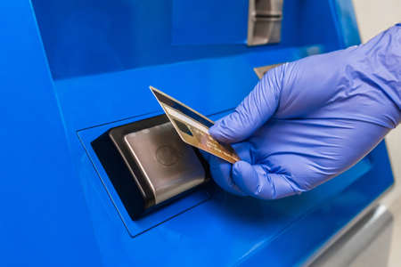 The hand of a person in a protective medical glove applies a bank card to the terminal and pays contactlessly.の写真素材