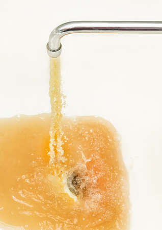 Rusty or dirty water flowing from a tap into a white bathtub or sink.の写真素材