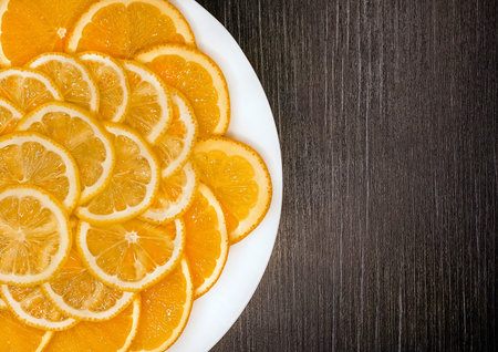 Sliced orange and lemon in a white plate on a dark wooden texture background, copy space.