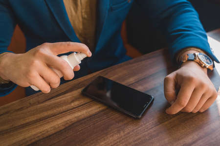 Businessman hands hold antiseptic and spray on phone screen on table background.の写真素材