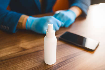 Antiseptic on the background of the hands of a businessman in protective medical gloves and a phone on the table.の写真素材