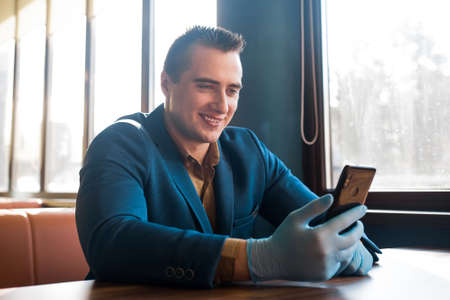 Young caucasian guy businessman in a blue suit and protective gloves looks into the phone and smiles.の写真素材