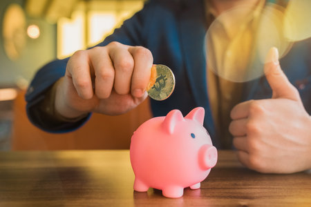 The hand of a businessman holds a golden bitcoin cryptocurrency next to a pig piggy bank. Bitcoin, cryptocurrency and savings concept.の写真素材