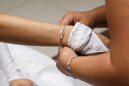 Mom's hand removes wedding glove from bride's daughter's hands close-up.の写真素材