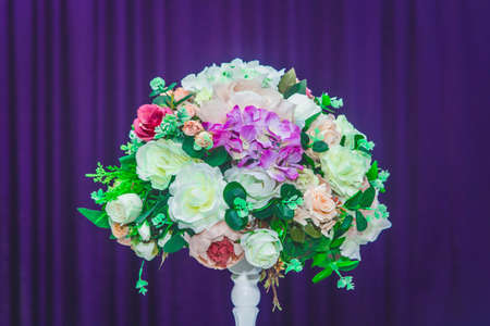 The element of wedding decoration is a bouquet of artificial flowers of roses in the interior of the room on background of purple curtain curtain.の写真素材