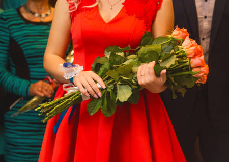 A girl witness in a red dress holds a bouquet of flowers rose close up at the wedding.の写真素材