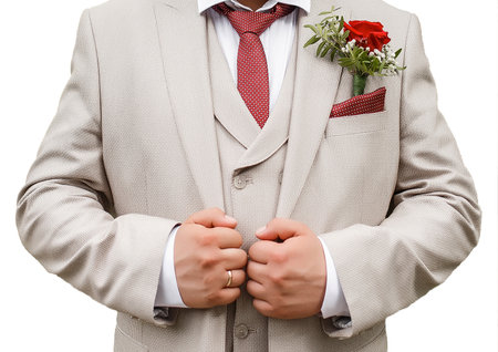 The groom's light beige suit holds hands with a boutonniere and a red tie isolated white background close-up.の写真素材