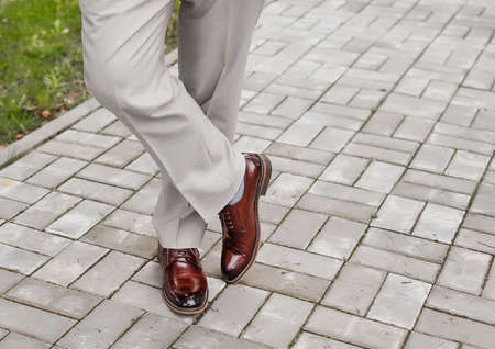 The man's legs are leg by foot in light trousers and brown shoes stand on paving tile.の写真素材