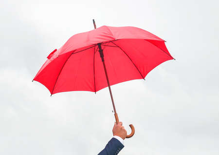 Man's hand holds red open umbrella against light sky.の写真素材
