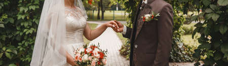 The groom in a brown suit holds the bride's hand with a wedding bouquet.の写真素材
